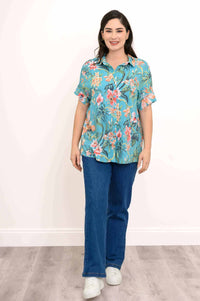Front view of woman modeling a teal floral blouse paired with jeans and white sneakers