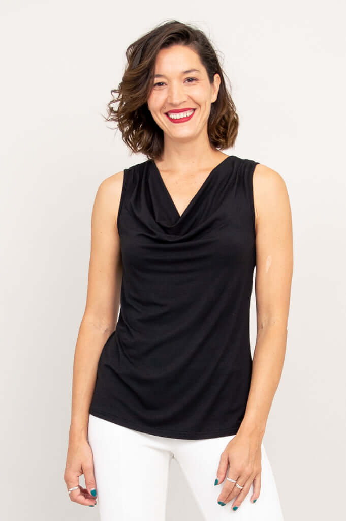Front view of a woman wearing a black sleeveless cowl neck top with white pants