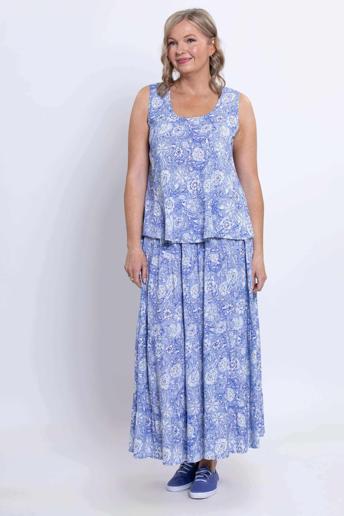 Fully body front view of woman wearing a sleeveless blue floral top on a long flowing matching skirt