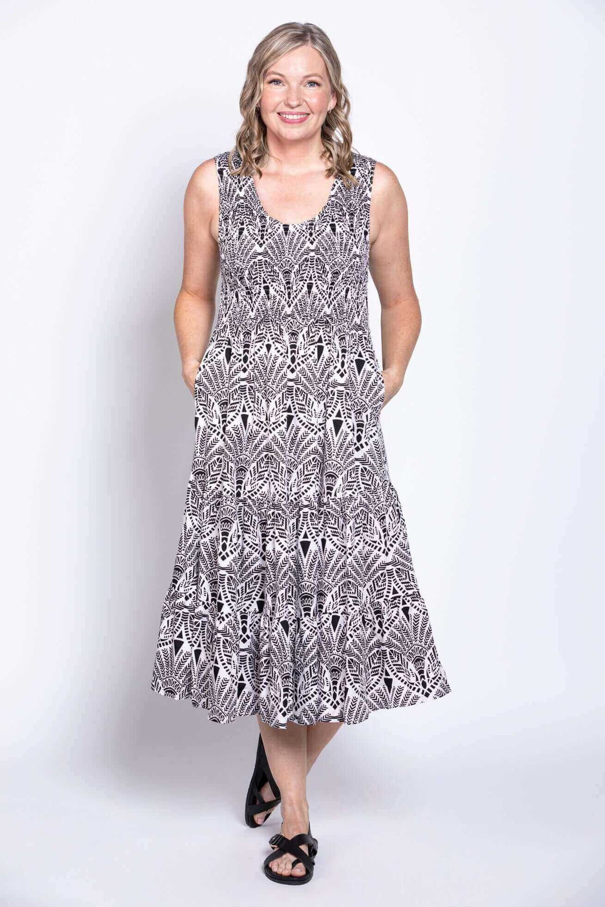 Front view of a woman wearing a sleeveless black and white printed tiered dress with pockets