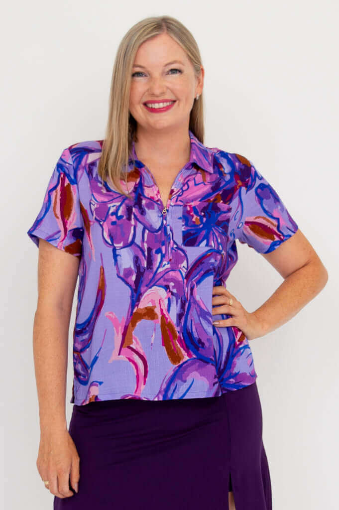 Front view of model wearing a vibrant purple abstract patterned short sleeve collared top