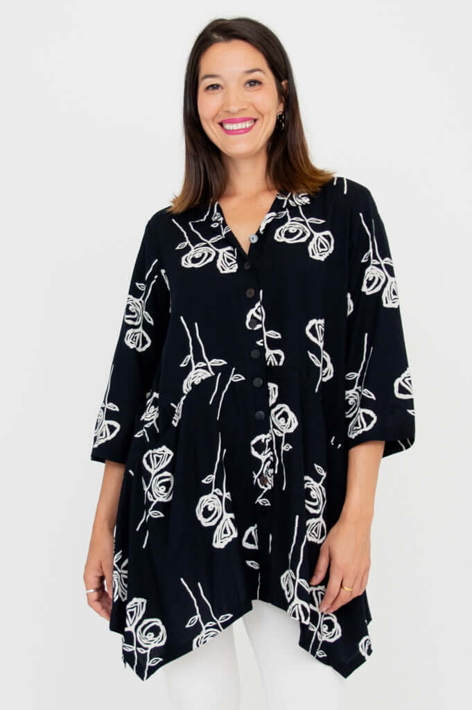 Woman wearing a black button-up tunic with white rose sketch print, front view