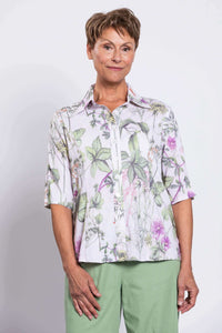 Close-up front view of woman wearing green floral button-up collared blouse and green pants