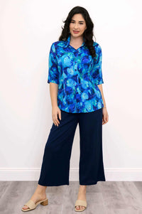 Full body view of woman wearing blue patterned button up blouse and dark blue pants