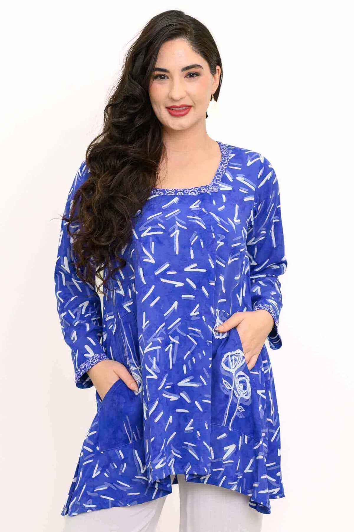 Front view of woman wearing a blue tunic with white abstract print and patch pockets