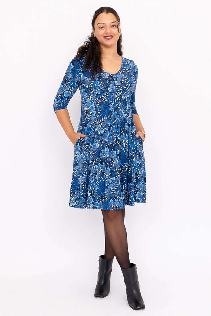 Front view of woman wearing a blue floral fit and flare dress with pockets and black ankle boots