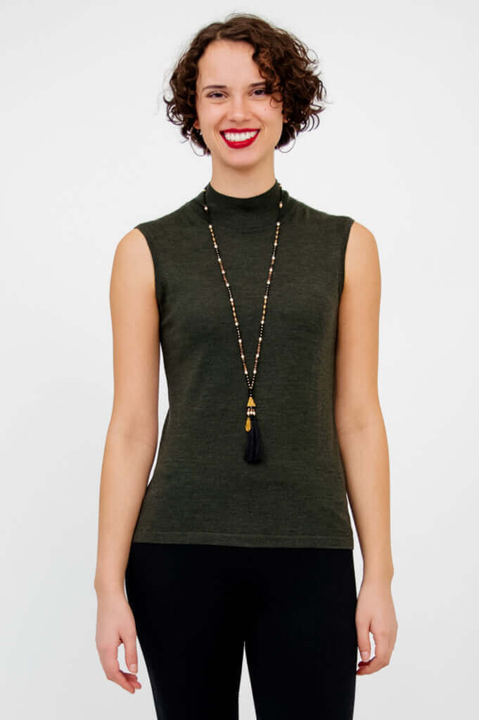 Woman wearing sleeveless olive-green mock neck sweater with long necklace, front view