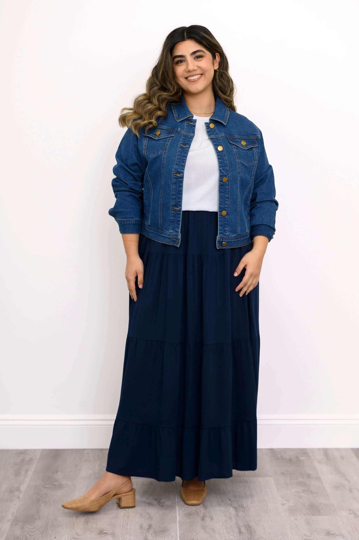 Model wearing a navy tiered maxi skirt with a white top and denim jacket, front view