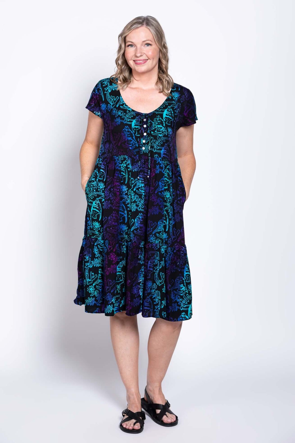 Woman modeling a black dress with flutter sleeves and blue-purple print, front view with hands in pockets