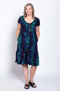 Woman modeling a black dress with flutter sleeves and blue-purple print, front view with hands in pockets