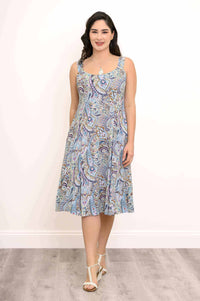 Front view of a woman in a blue paisley print sleeveless A-line dress, standing against a white wall