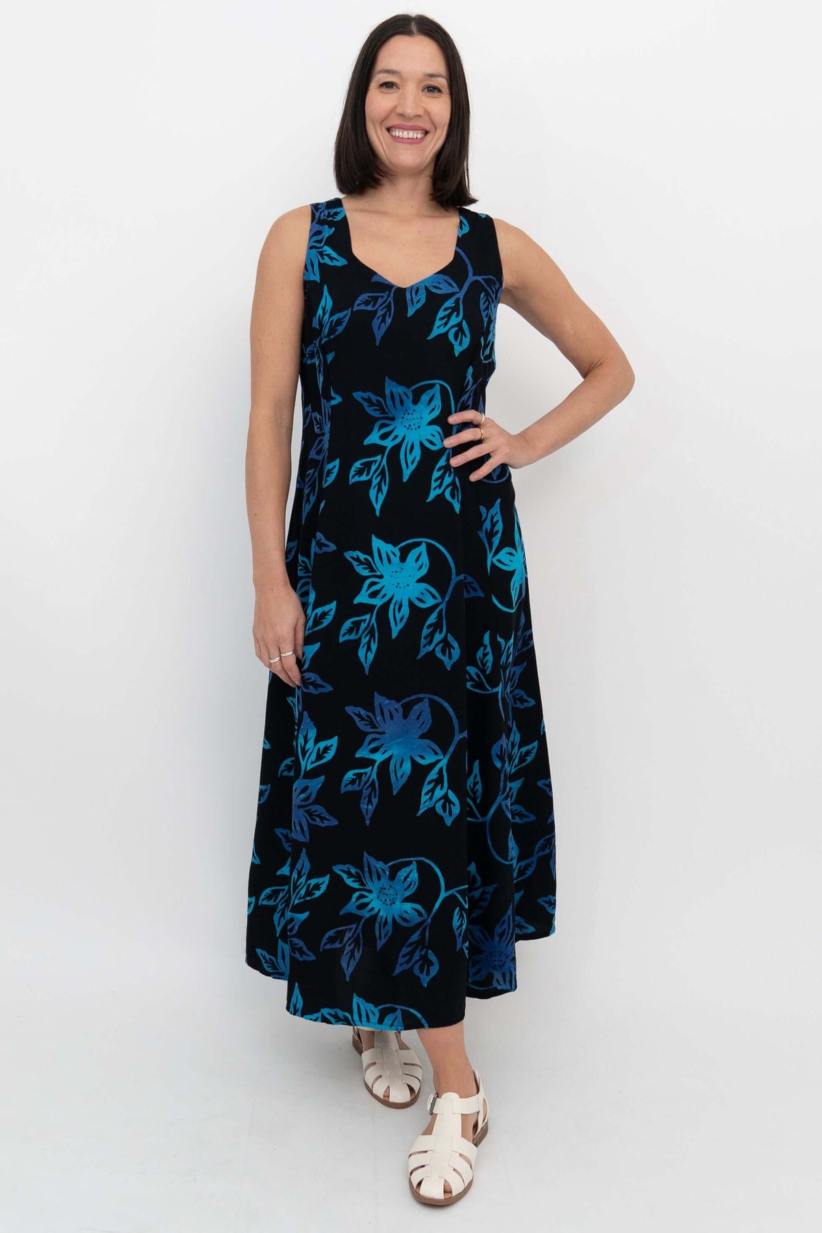 Woman wearing a sleeveless black and blue floral A-line dress, standing and smiling