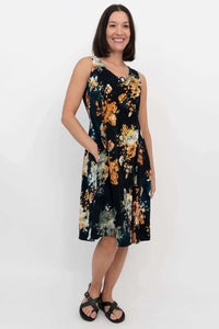 Woman wearing a sleeveless, black floral A-line dress with pockets, facing forward