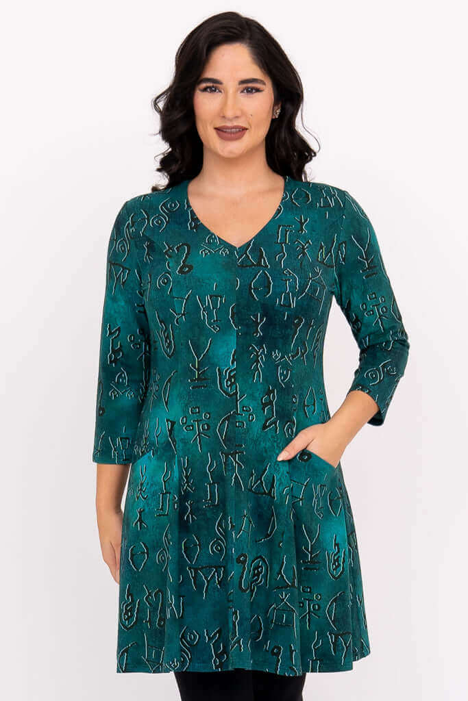 Front view of a woman wearing a teal abstract print v-neck bamboo tunic dress with front pockets.
