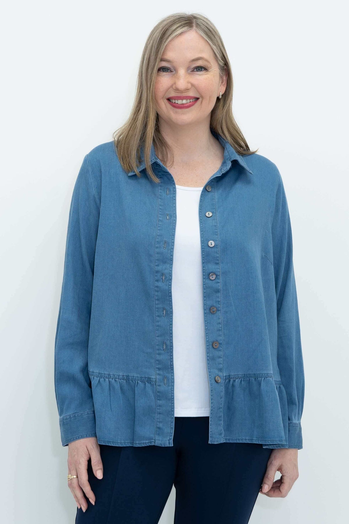 Front view of a woman wearing a blue Tencel denim blouse with ruffled hem