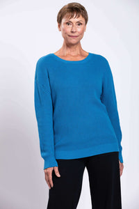 Front view of a woman wearing a relaxed blue knit sweater and black pants