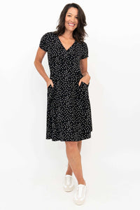 Front view of woman wearing a black and white polka dot crossover dress with short sleeves and pockets