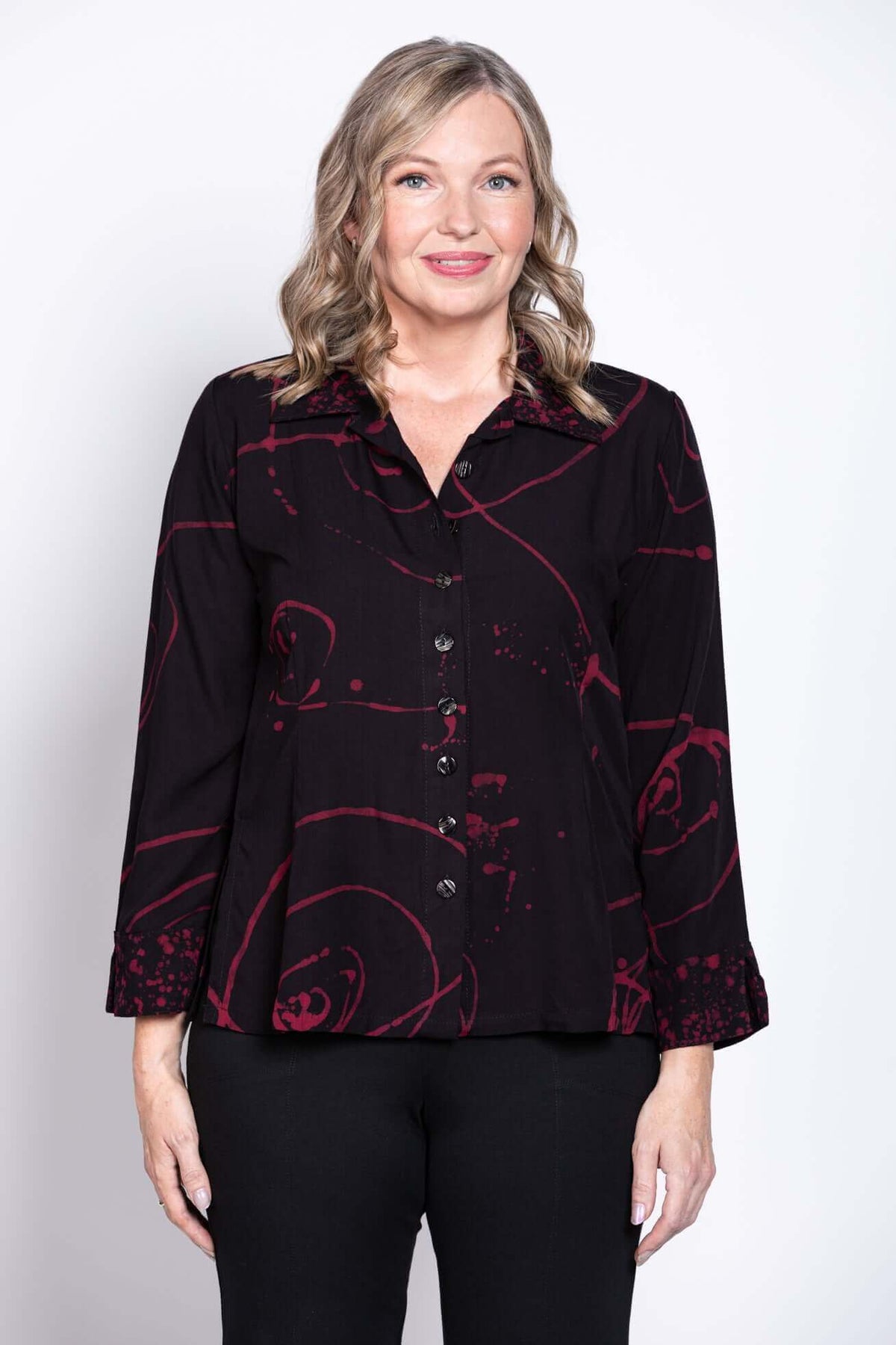 Front view of a woman wearing a black button-front blouse with red abstract print