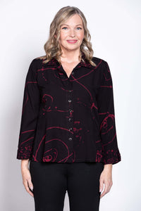 Front view of a woman wearing a black button-front blouse with red abstract print