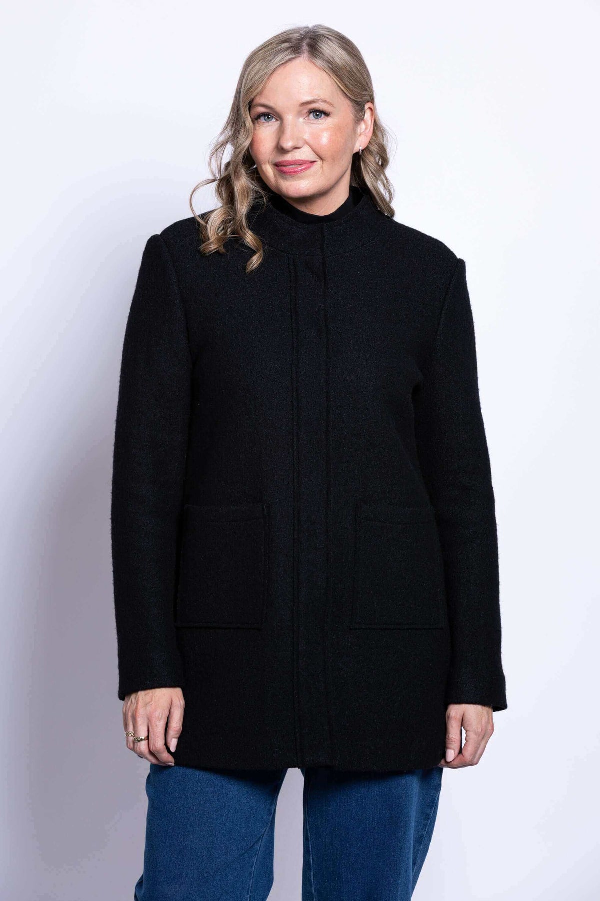 Front view of a woman wearing a black boiled wool coat with patch pockets
