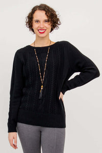 Front view of a woman in a black cotton cable knit sweater with boatneck and ribbed hem
