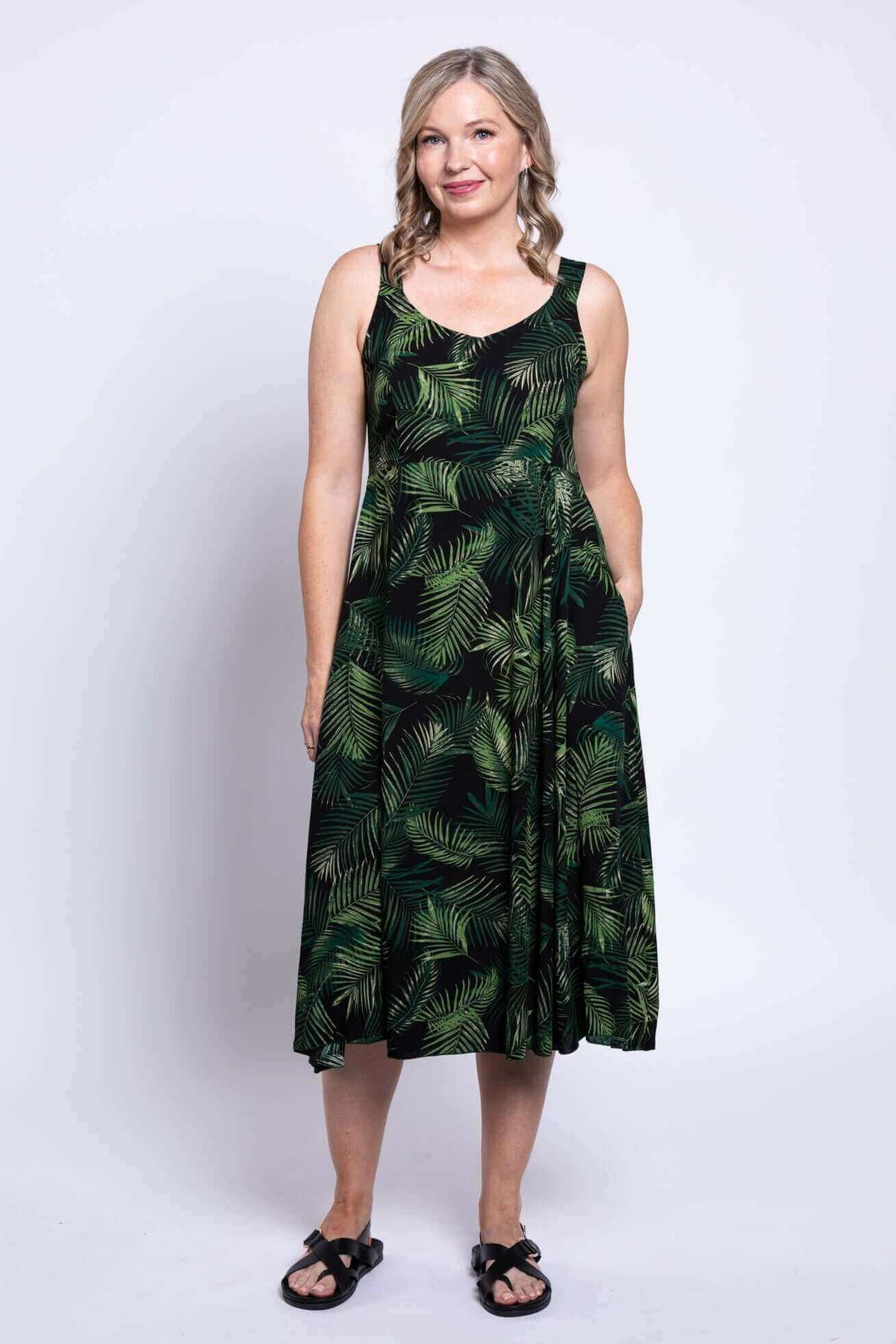 Front view of woman in black dress with green tropical leaf pattern and pockets