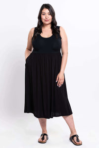 Front view of a woman wearing a black sleeveless empire waist midi dress with pockets