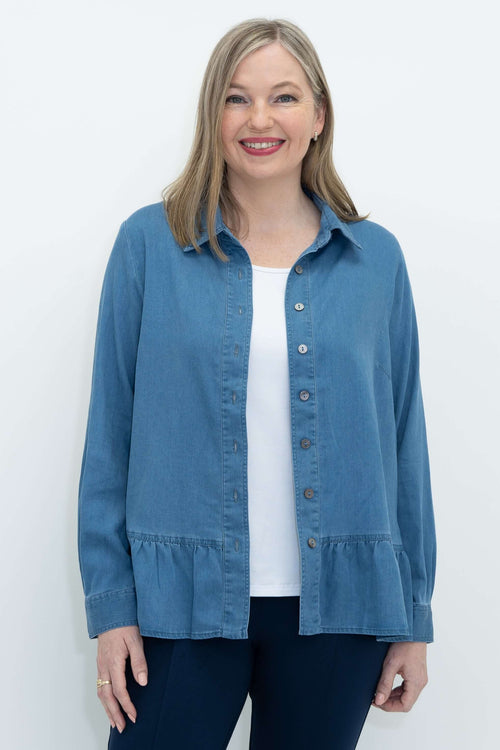 Front view of a woman wearing a blue Tencel denim ruffle blouse with button closure