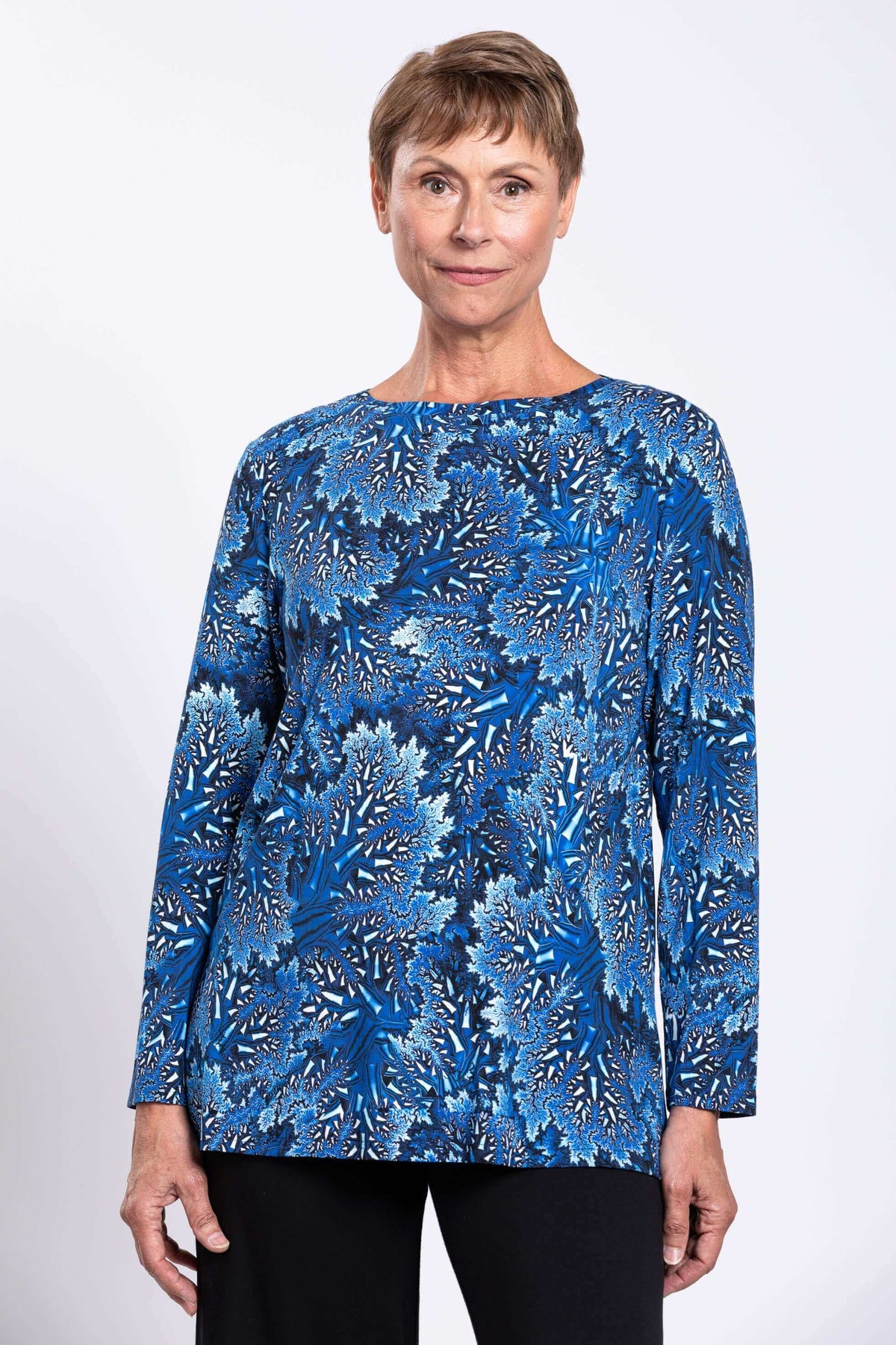 Close up front view of a woman wearing a blue botanical print bamboo top with a boat neckline.
