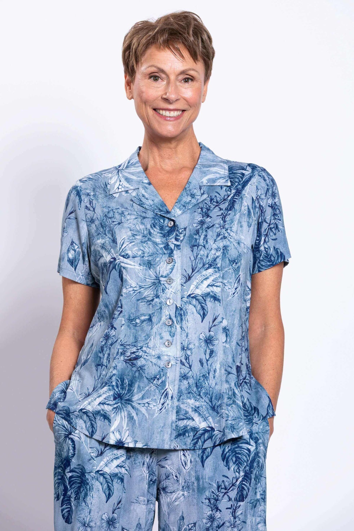 Front view of woman wearing a blue botanical print short sleeve shirt and matching pants