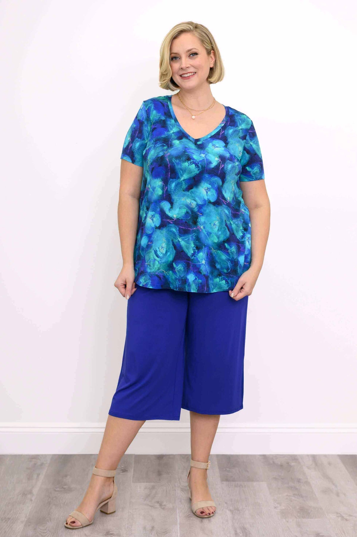 Woman smiling, wearing a blue floral V-neck top and blue crop pants