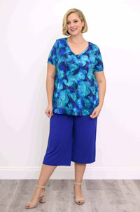 Woman smiling, wearing a blue floral V-neck top and blue crop pants