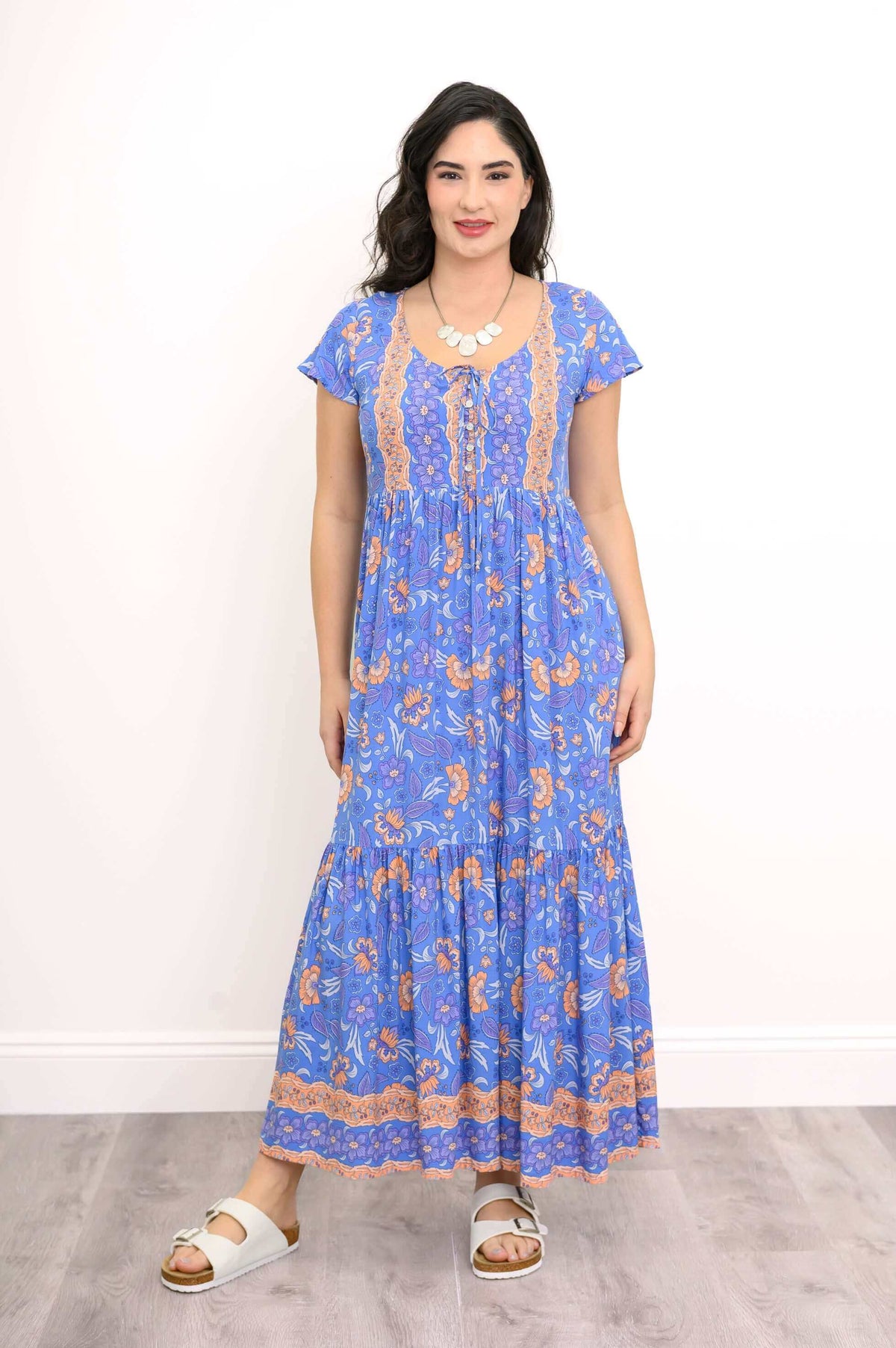 Front view of woman wearing a blue floral boho maxi dress with peach accents and cap sleeves