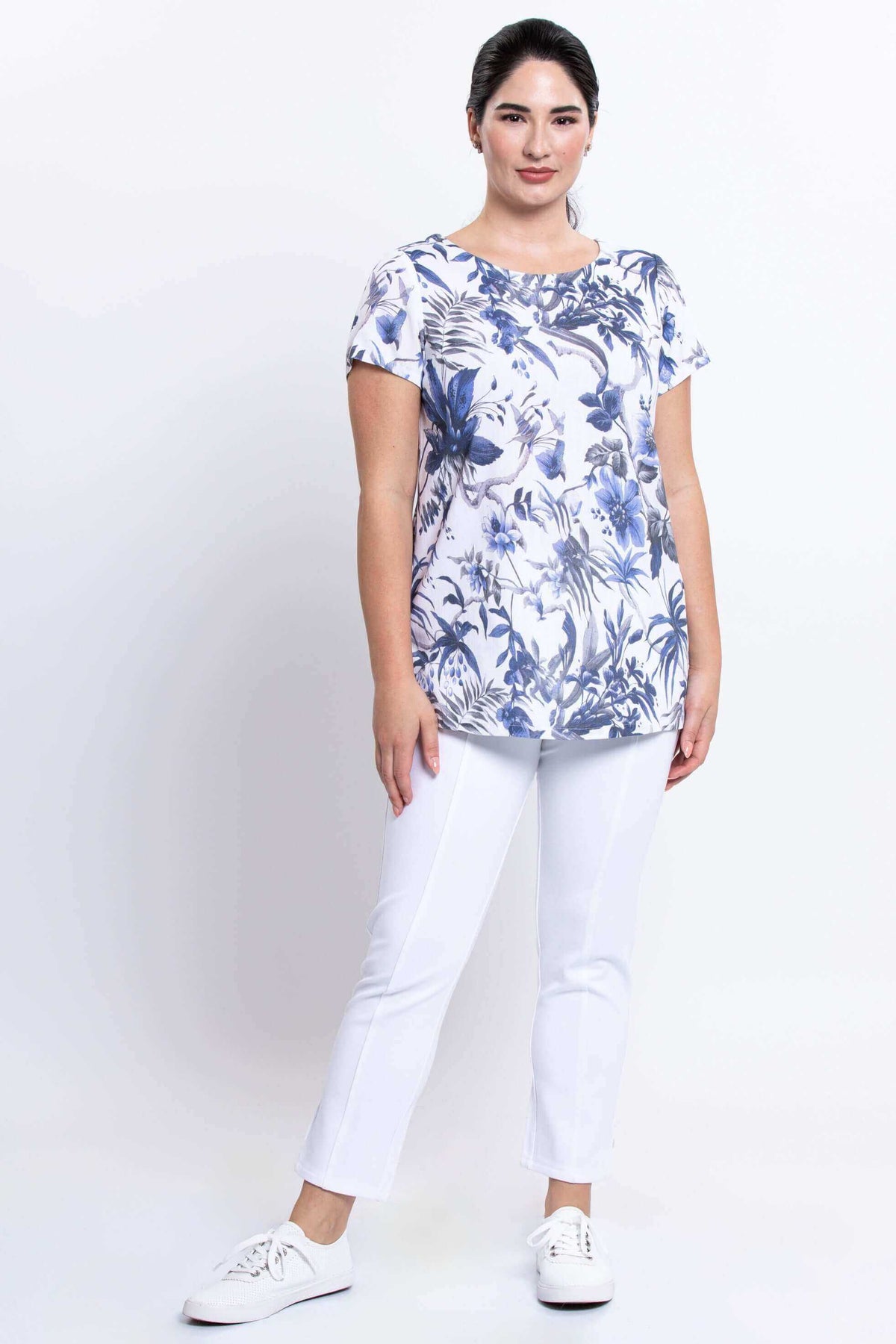 Woman in blue floral top paired with white pants and white sneakers, front view