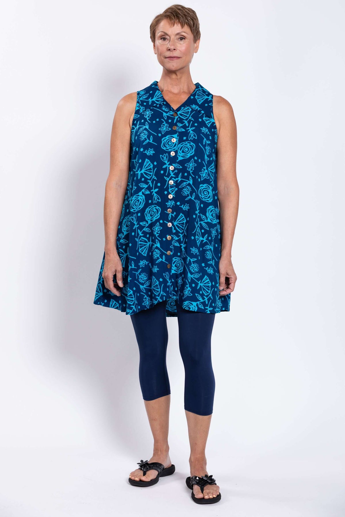 Front view of woman wearing blue sleeveless floral button-up tank dress with leggings