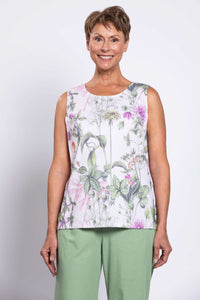Smiling woman in a botanical print tank top and light green pants, front view