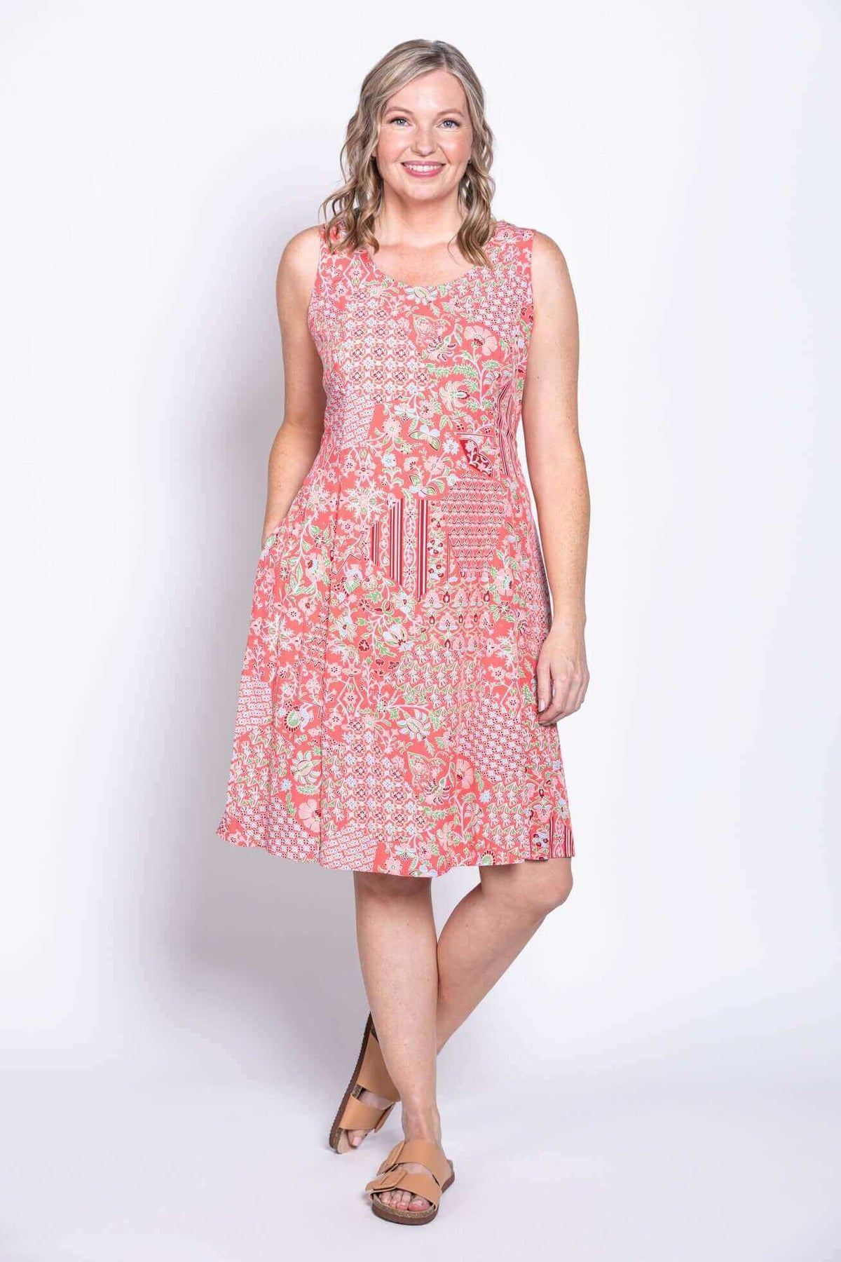 Woman smiling in a coral floral sleeveless A-line dress with patchwork patterns, front view