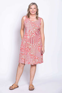 Woman in a coral floral patchwork summer dress, standing with hands in pockets, front view