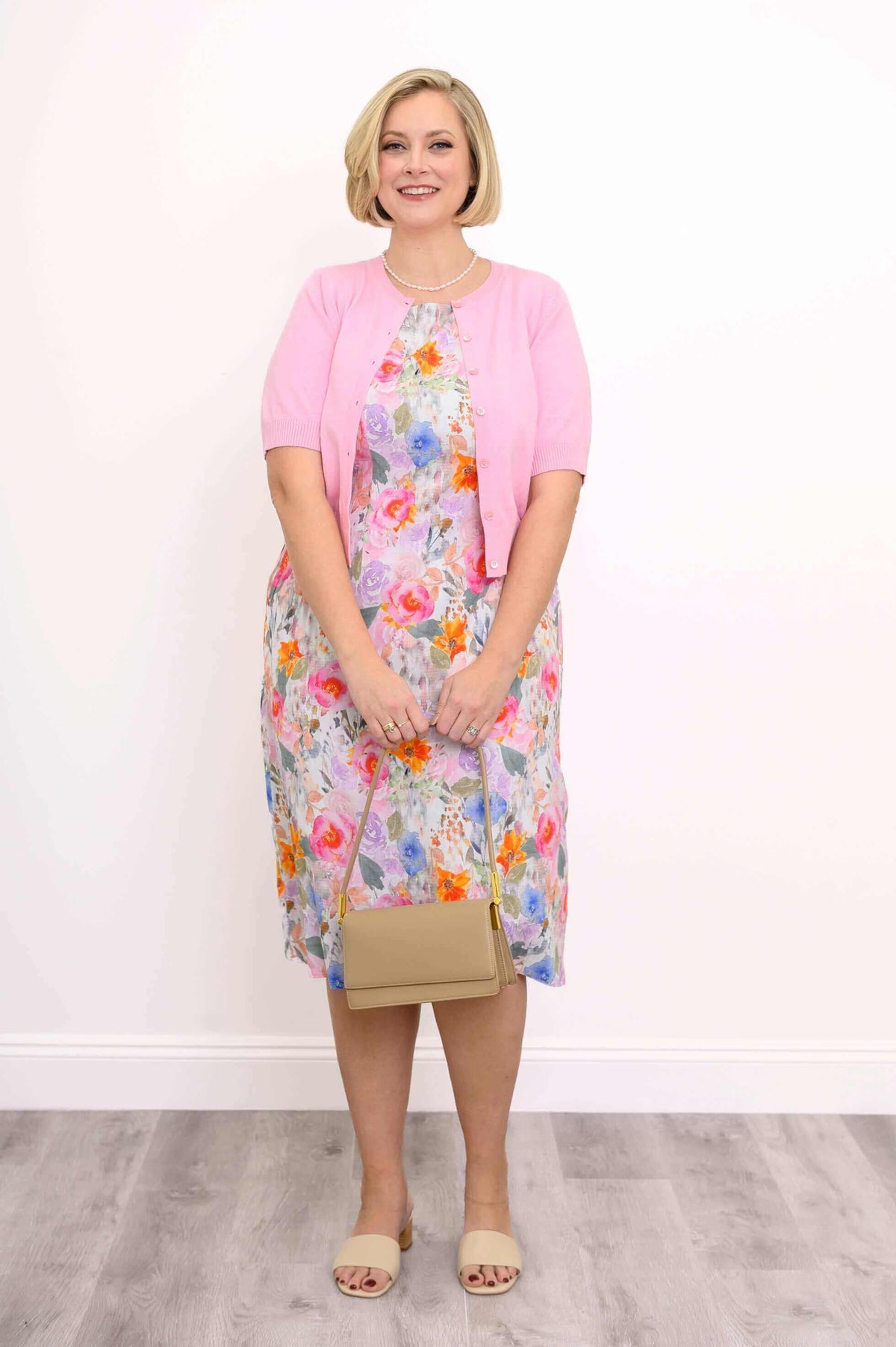 Front view of floral shift dress with pink cardigan and pearl necklace
