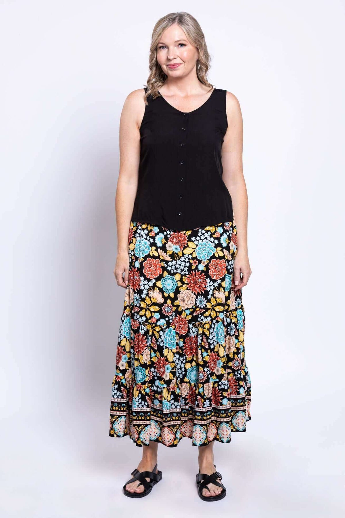 Front view of a woman in a sleeveless black top and floral tiered maxi skirt