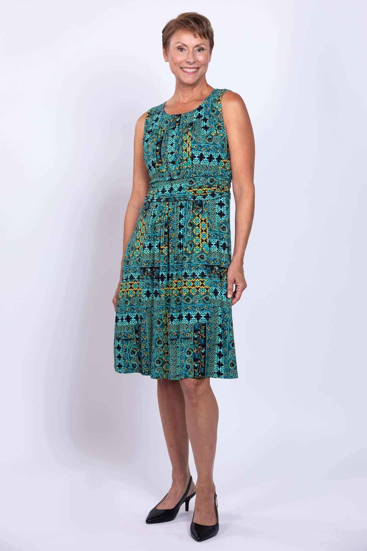 Woman smiling in teal and yellow geometric patterned sleeveless dress
