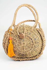 Front view of hand woven rattan bag with orange pom-pom and round handles