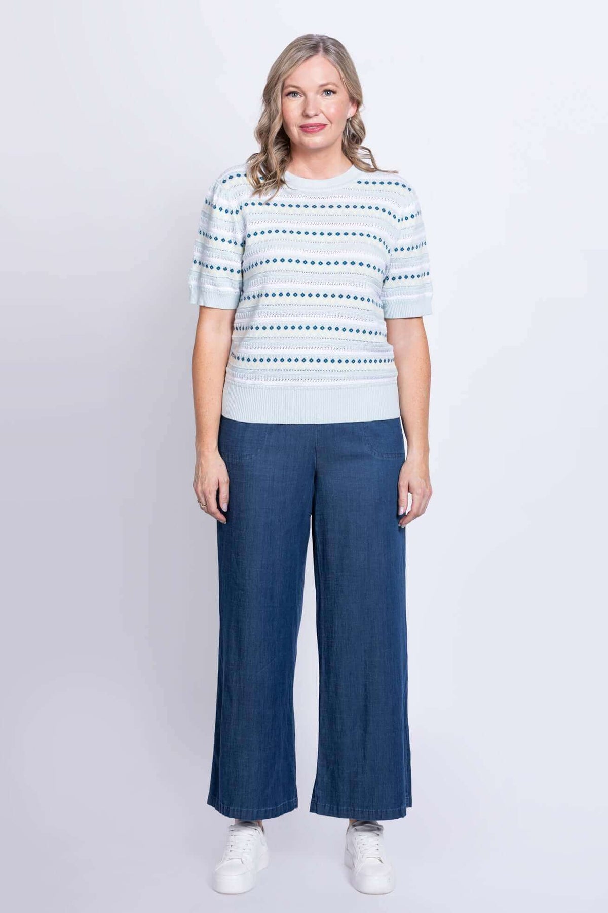 Woman in light blue patterned sweater and wide-leg jeans, front view
