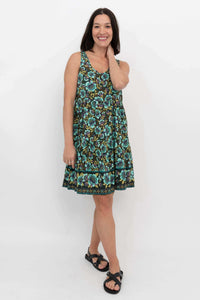 Woman wearing sleeveless tiered dress with green and blue floral print, smiling