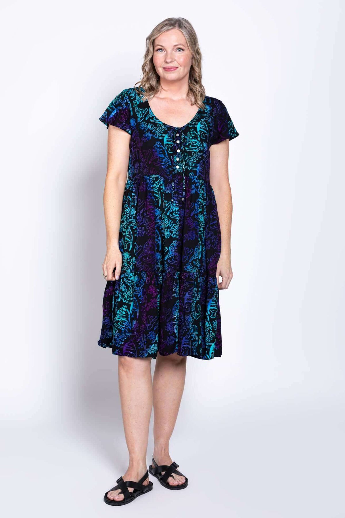 Front view of model wearing a black dress with teal and purple botanical print and flutter sleeves