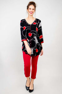 Front view of model in batik-patterned black top with red shapes, red pants, and heels