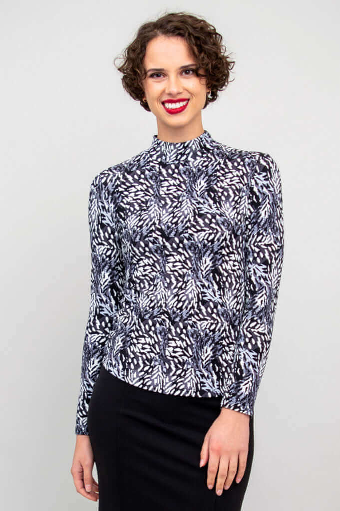 Woman wearing a fitted black and white palm print mock neck top and black skirt, facing forward