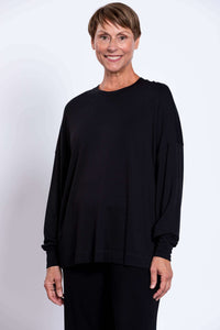 Front view, model wearing loose black crew neck top with full sleeves