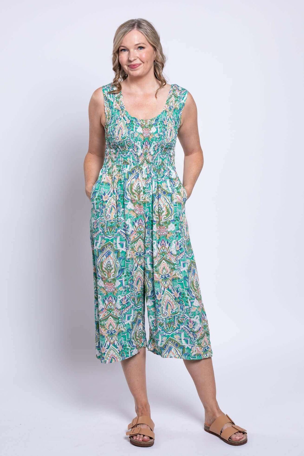 Front view of model wearing a green and blue paisley shirred jumpsuit with wide legs