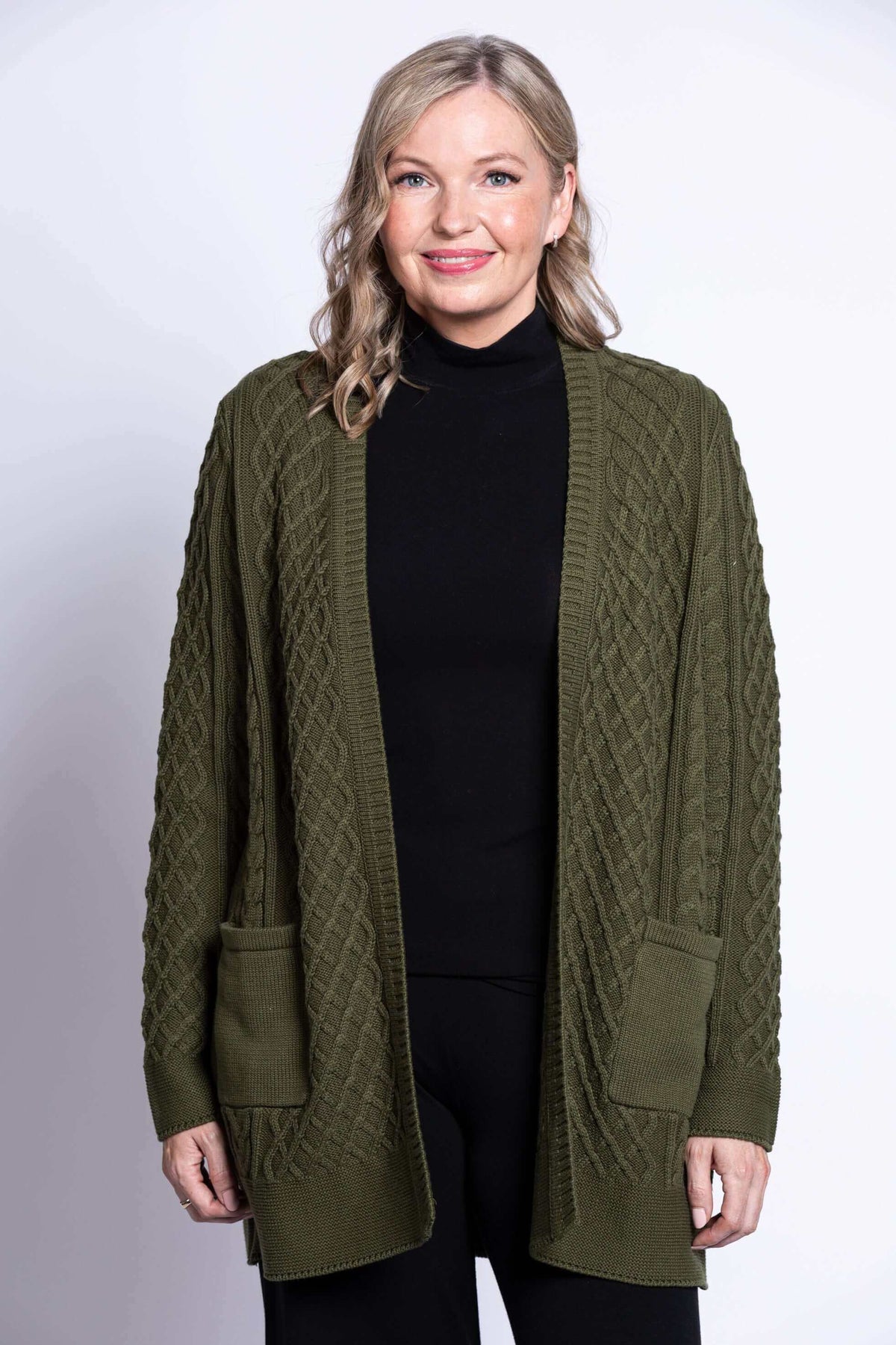 Front view of a woman wearing an olive green cable knit cardigan with patch pockets
